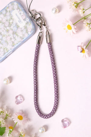 Purple phone strap with floral phone case and flowers on a light pink background